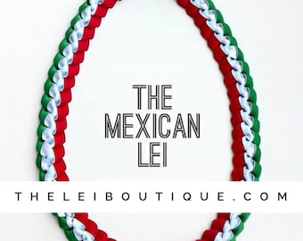 May include: A green, white, and red ribbon lei with a bow at the top. The lei is made of multiple strands of ribbon that are woven together. The text "THE MEXICAN LEI THELEIBOUTIQUE.COM" is printed below the lei.