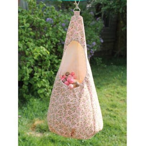 May include: A pink fabric hanging bird feeder with a floral pattern and a large oval opening. The feeder is filled with small, colorful balls and is suspended from a green line with a silver clasp.