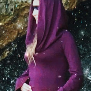 May include: A deep purple hooded top with long sleeves. The hood drapes over the shoulders. The person is wearing sunglasses. The background is a dark, speckled pattern with sparkling effects.
