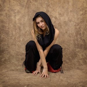 May include: A black hooded garment with a cowl neckline and loose-fitting black trousers featuring red inner lining at the cuffs and adjustable side drawstrings. The outfit consists of a soft fabric construction with a draped hood and wide-leg pants.