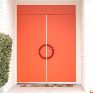 May include: A pair of bright orange double doors with a circular red door handle. The doors are set in a white frame and lead to a white tiled entryway.