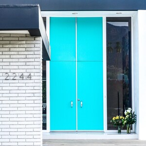 Puede incluir: Un edificio de ladrillo blanco con una doble puerta turquesa y un panel de vidrio a la derecha. La puerta tiene dos manijas plateadas y el número "2244" está escrito en la pared de ladrillo.