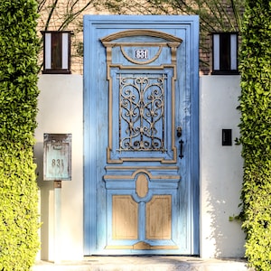 Peut inclure: Une porte en bois bleu avec une grille métallique décorative et un numéro de maison en laiton "831" au-dessus. La porte a une bordure brun clair et un aspect vieilli.