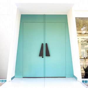 May include: A pair of teal double doors with black triangular door handles. The doors are set in a white frame with a white wall behind them.