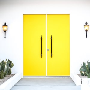 May include: A pair of bright yellow double doors with black door handles, set against a white wall with two black wall sconces on either side.