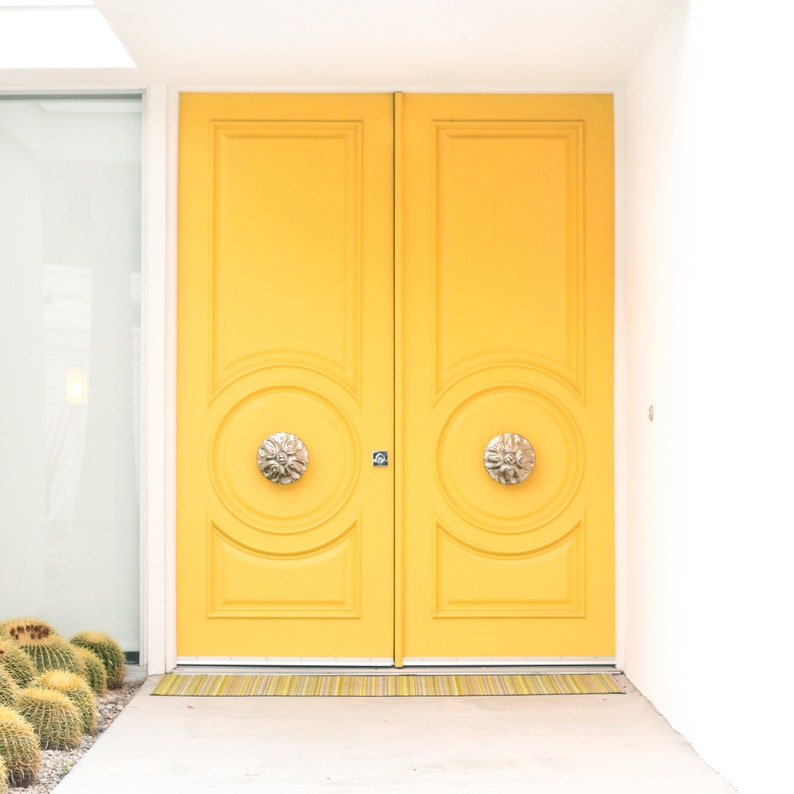 May include: A pair of bright yellow double doors with ornate brass door knobs. The doors are set in a white frame and have a yellow doormat.