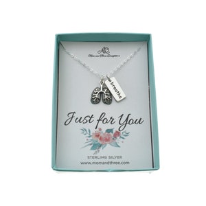 May include: A sterling silver necklace with a lung charm and a rectangular tag that says "breathe". The necklace is presented in a teal box with the words "Just for You" and a floral design.