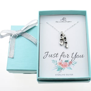 May include: A silver necklace with ballet slipper charms is displayed inside a light blue gift box tied with a silver ribbon. The card inside the box reads "Just for You" with floral accents and "Sterling Silver" text.