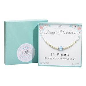 May include: A necklace with 16 pearls, presented in a gift box. The necklace has a central blue crystal and is accompanied by a card that reads "Happy 16th Birthday!" and "16 Pearls one for each fabulous year." The box is light blue.