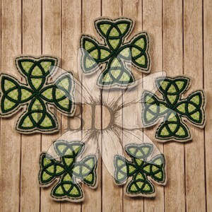 May include: Five green and white Celtic knot cross patches on a wood background.