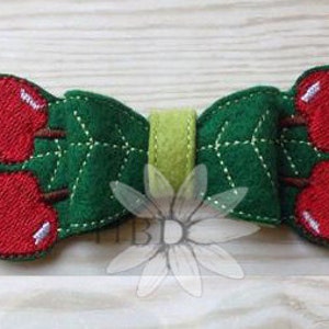 May include: A green felt bow with two red cherries on each side. The bow is decorated with a green felt leaf pattern.