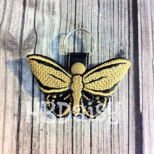 May include: A gold and black butterfly keyring with a black leather strap and a silver key ring.