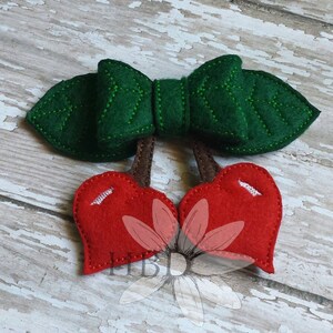 May include: A felt cherry applique with a green bow and brown stems. The cherries are red and have a heart shape.