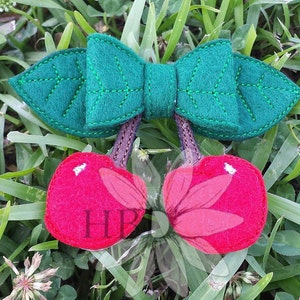 May include: A felt cherry bow with green leaves and red cherries. The bow is tied with a brown ribbon.
