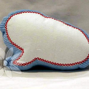 Puede incluir: Una almohada azul y roja bordada con forma de bocadillo. La almohada está hecha de una tela suave y mullida y tiene un centro blanco.