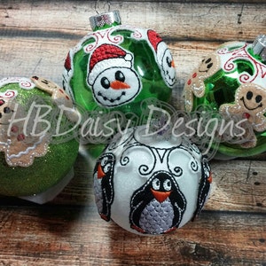 May include: Four Christmas ornaments with different embroidered designs. One ornament is green with a snowman design, one is white with a penguin design, and two are green with gingerbread men designs.
