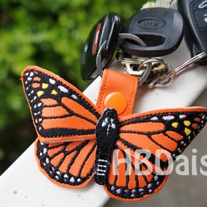 May include: Orange and black butterfly keyring with a black and white embroidered design. The keyring is attached to a set of keys with a silver key ring.