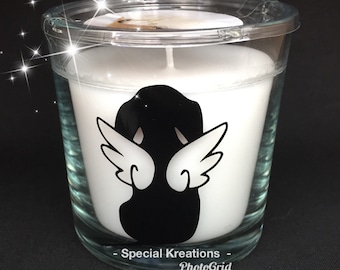 May include: A clear glass votive candle holder with a white candle inside. The candle holder has a black silhouette of an angel with white wings. The text "- Special Kreations - PhotoGrid" is printed on the bottom of the glass.