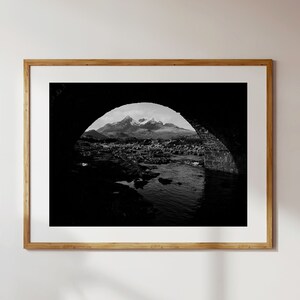 Puede incluir: Una fotografía en blanco y negro de un arco de piedra con vista a una cordillera en la distancia. El arco es oscuro y la cordillera es clara.