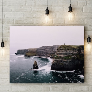 May include: A photograph of the Cliffs of Moher in Ireland. The cliffs are tall and rugged, with a small tower on top. The ocean is a deep blue, and the sky is a light grey. The photo was taken from a distance, so the cliffs appear small in the frame.