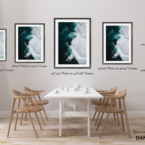 May include: A collection of framed art prints depicting an aerial view of ocean waves. The prints vary in size, with the largest being 36x24 inches in a 40x28 inch frame. The artwork features shades of teal and white, creating a dynamic contrast. The prints are displayed above a dining table.