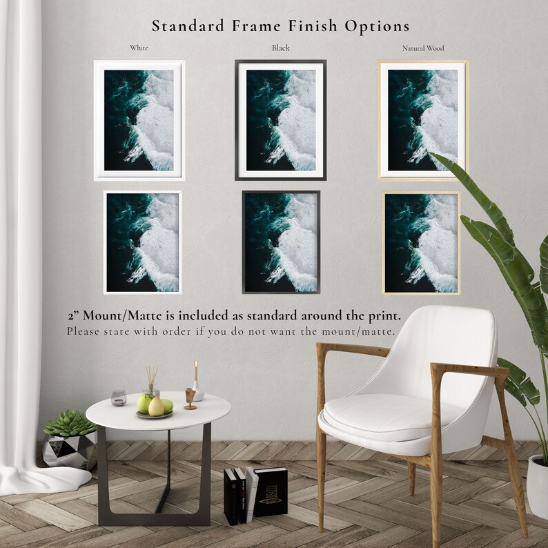 May include: A display of framed art prints showcasing ocean wave imagery. Frames are available in white, black, and natural wood finishes. The text indicates a 2-inch mount/matte is standard. The room setting includes a white chair and a small table.