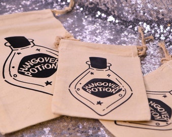 May include: Three beige drawstring pouches made of fabric, each featuring a black graphic print of a potion bottle with a cork stopper. The text "HANGOVER POTION" is printed in black inside the bottle shape, surrounded by small star icons.