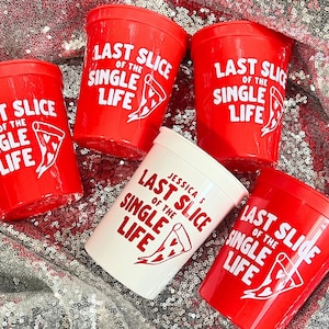 May include: Red plastic cups with the text "LAST SLICE OF THE SINGLE LIFE" and a pizza slice graphic in white. One white cup has the text "JESSICA'S LAST SLICE OF THE SINGLE LIFE". The cups are on a sequined surface.