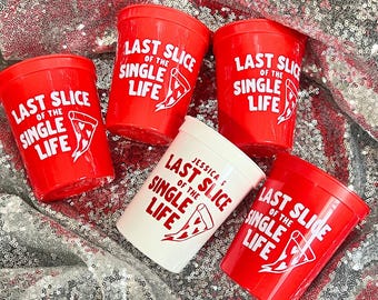 May include: Red plastic cups with the text "LAST SLICE OF THE SINGLE LIFE" and a pizza slice graphic in white. One white cup has the text "JESSICA'S LAST SLICE OF THE SINGLE LIFE". The cups are on a sequined surface.