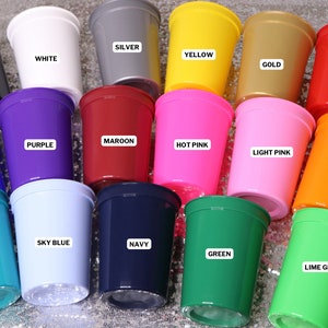 Op de afbeelding: Een verzameling plastic bekers in verschillende kleuren, waaronder zwart, wit, zilver, geel, goud, rood, paars, kastanjebruin, felroze, lichtroze, koningsblauw, oranje, hemelsblauw, marineblauw, blauwgroen, groen en limoengroen. Elke beker is voorzien van een label met de kleurnaam.