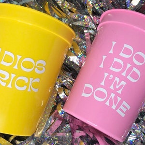 May include: Two plastic cups with white text. The yellow cup says "ADIOS PRICK" and the pink cup says "I DO I DID I'M DONE".