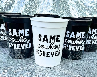 May include: A collection of plastic stadium cups in black and white, each featuring the text SAME cowboy FOREVER with a ring icon replacing the letter O in the word FOREVER. The cups are arranged in a group, displaying contrasting color schemes.