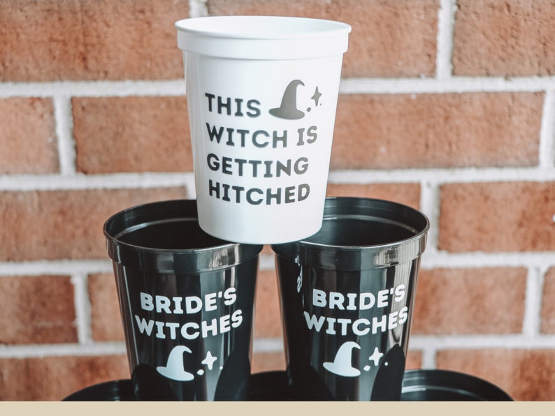May include: White and black plastic cups with witch-themed text and graphics. One cup reads "THIS WITCH IS GETTING HITCHED" with a witch hat and star. Other cups say "BRIDE'S WITCHES" with a witch hat and star. The cups are stacked.