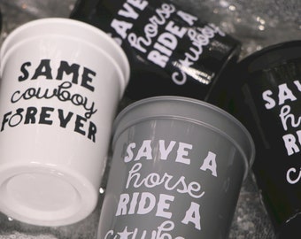 Puede incluir: Un conjunto de tazas blancas, grises y negras con texto blanco. La taza blanca dice "SAME cowboy FOREVER". La taza gris dice "SAVE A horse RIDE A cowboy". Las tazas negras dicen "SAVE horse RIDE A cowboy."