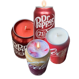 May include: Four red and yellow soda can candles with flames. The candles are labeled "Dr Pepper" and "Coca-Cola".