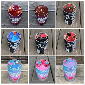 Może przedstawiać: Kolekcja dziewięciu świec umieszczonych w puszkach po napojach, w tym wzory Dr. Pepper, Oreo i Coca-Cola Y3000. Każda świeca ma kolorową warstwę wosku na g&oacute;rze, ozdobioną r&oacute;żnymi suszonymi kwiatami, płatkami i elementami botanicznymi.