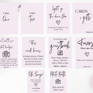 May include: Pink and white wedding signage with calligraphy text. The signs include table numbers, a photo booth sign, a guest book sign, a sign for favours, a sign for cards and gifts, and a sign that says "Light up the dance floor".