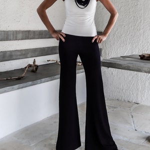 May include: A woman wearing a white tank top with a black scarf and black wide-leg pants. She is wearing sunglasses and has blonde hair.