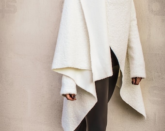 May include: A white, fuzzy, asymmetrical wrap with long sleeves and a high neckline. The wrap is worn over black leggings and black heeled boots.