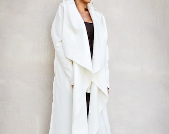 May include: A white long-sleeved coat with a draped collar and a long, flowing design. The coat is worn over black leggings and black heeled ankle boots.