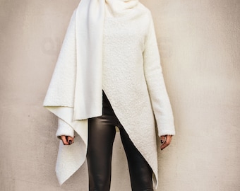 May include: A white, fuzzy, asymmetrical sweater with a cowl neck and long sleeves. The sweater is worn with black leather leggings and black heeled boots.