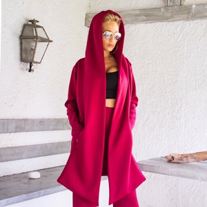 Op de afbeelding: Een vrouw draagt een magenta hoodie en een bijpassende wijde broek. De hoodie heeft een lang, vloeiend ontwerp en de broek heeft een uitlopende pasvorm.