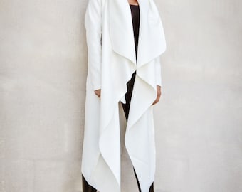 May include: A white long-sleeved coat with a draped collar and a long, flowing design. The coat is worn over black pants and black heeled boots.
