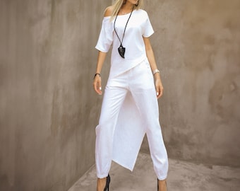 May include: A white linen outfit consisting of an asymmetrical top and wide-leg pants. The top has an off-the-shoulder design, and the pants feature a unique split front. The outfit is paired with black high heels and a long black necklace.