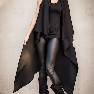 May include: A black long vest with a draped design, worn over a black tank top and black leggings. The model is wearing black heeled boots.