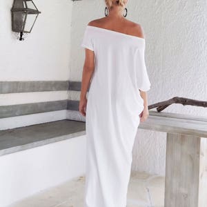 May include: A floor-length white dress with an off-the-shoulder neckline and short sleeves. The garment features a loose, flowing silhouette that drapes down to the floor, providing a relaxed fit. The fabric is solid white with no patterns.