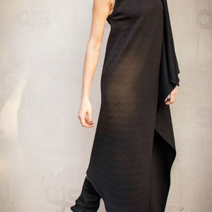 May include: A black sleeveless dress with a high neck and a long, flowing skirt. The dress has a quilted texture and a draped design. The model is wearing black boots.