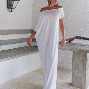 May include: A floor-length white dress with an off-the-shoulder neckline and short sleeves. The garment features a loose, flowing silhouette that extends to the floor, crafted from a solid white fabric with a smooth, opaque finish throughout.