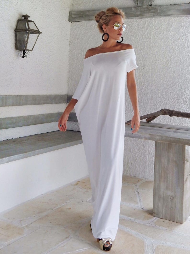 May include: A floor-length white dress with an off-the-shoulder neckline and short sleeves. The garment features a loose, flowing silhouette that extends to the floor, crafted from a solid white fabric with a smooth, opaque finish throughout.