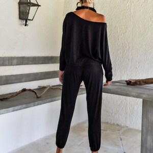 May include: A woman wearing a black off-the-shoulder jumpsuit with a relaxed fit. The jumpsuit has long sleeves and a slightly cropped leg. She is wearing black high heels.